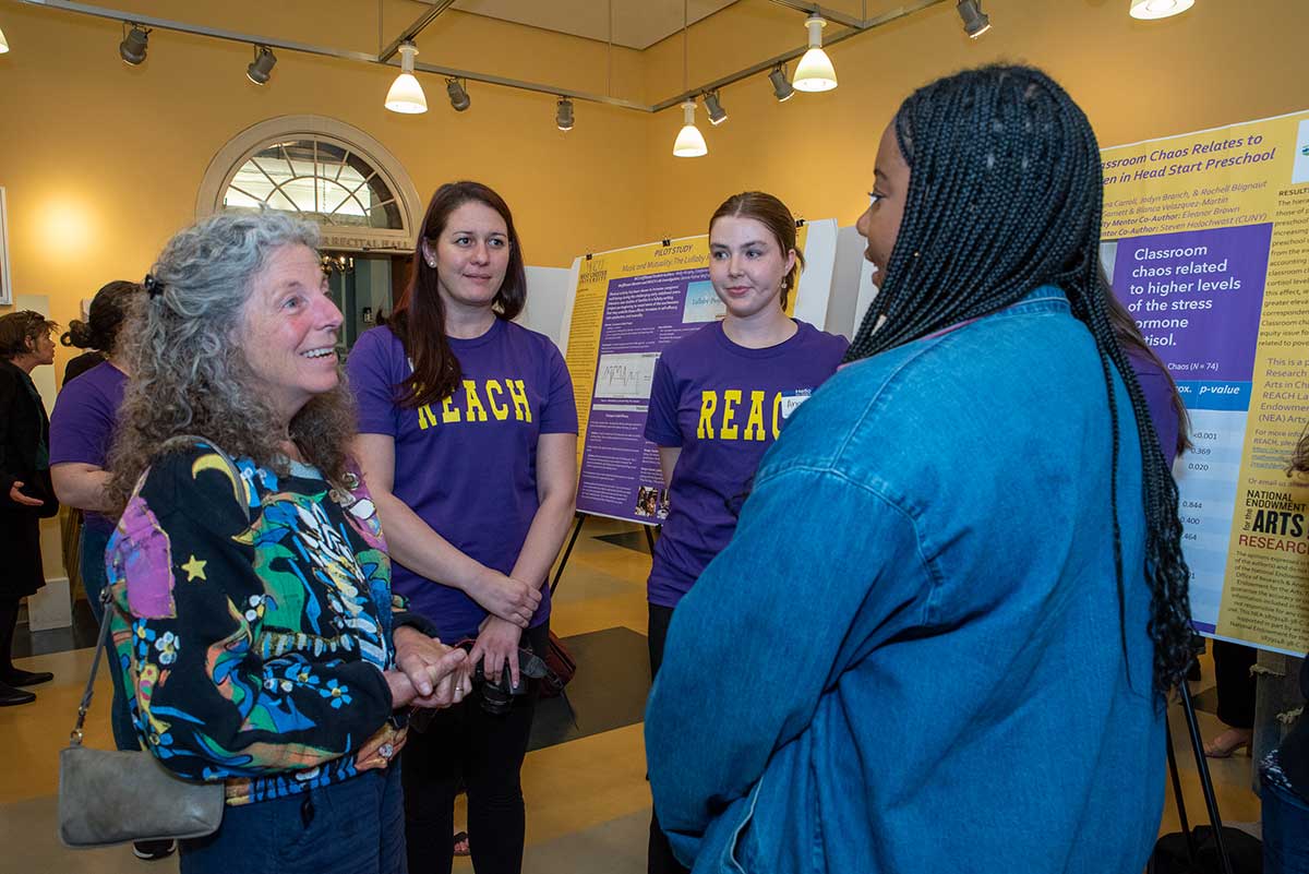 Jan Michener, Director of Arts Holding Hands and Hearts (AHHAH), talks with WCU Psychology BS students Rochell Blignaut, Anna Carroll, and Jadyn Branch about their research poster on classroom chaos and child cortisol levels.