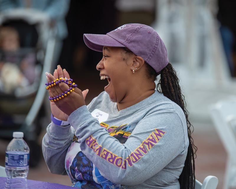 Young woman in WCU gear happy and clapping with purple and yellow beads