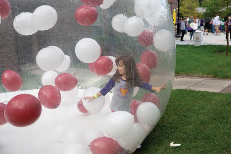 little girl is playing in the blow up bubble with balloons