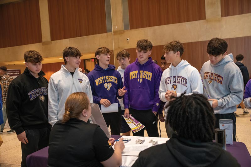 a group of WCU boys in WCU gear getting information from a booth at an event