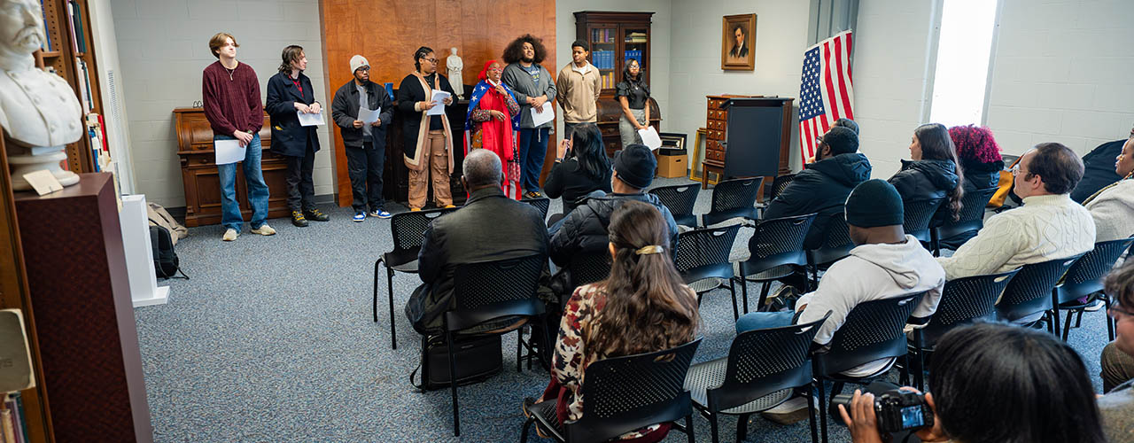 Photo from the back of the room at event with multiple participants sitting and watching presentation
